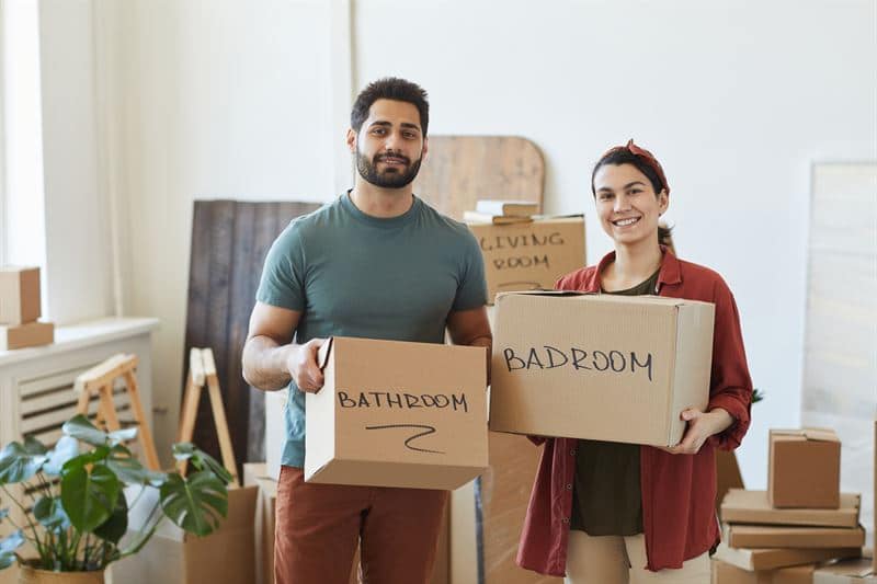 A man and a woman holding packed up boxes - one saying bathroom and the other saying bedroom.