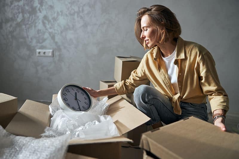 A woman moving into her home and unpacking a clock from a box.