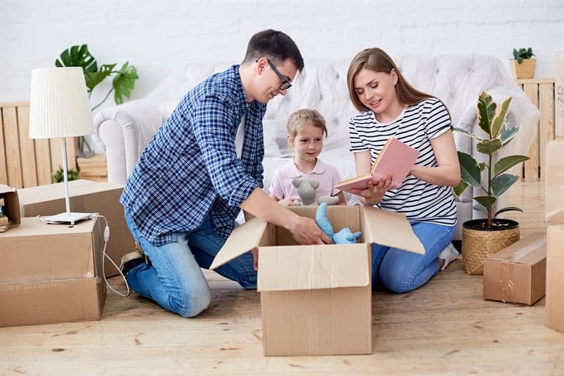 Adult parents with their young toddler unpacking a box in their new home