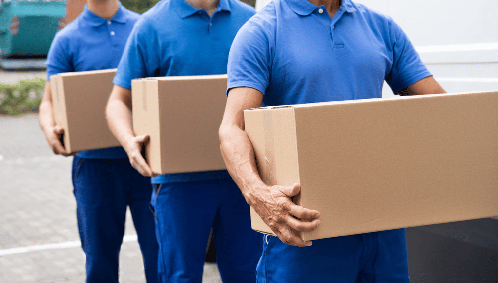 Three men in blue shirts holding packing boxes